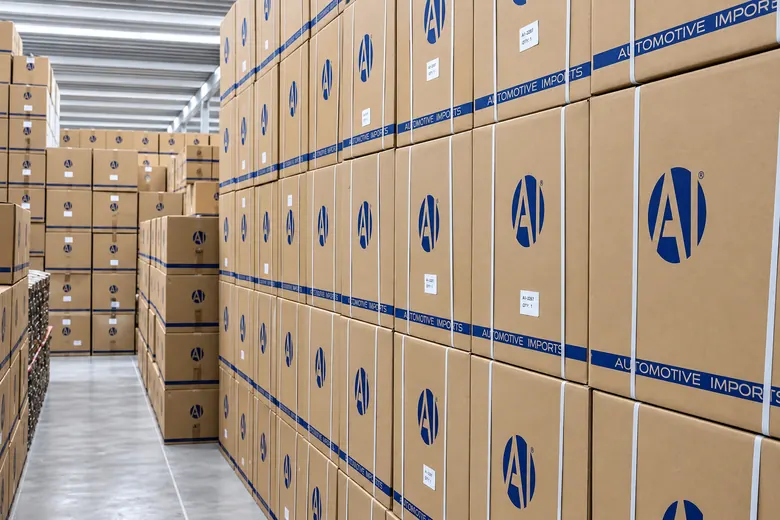 Paredão de caixas Automotive Imports empilhadas e etiquetadas, num corredor de estoque